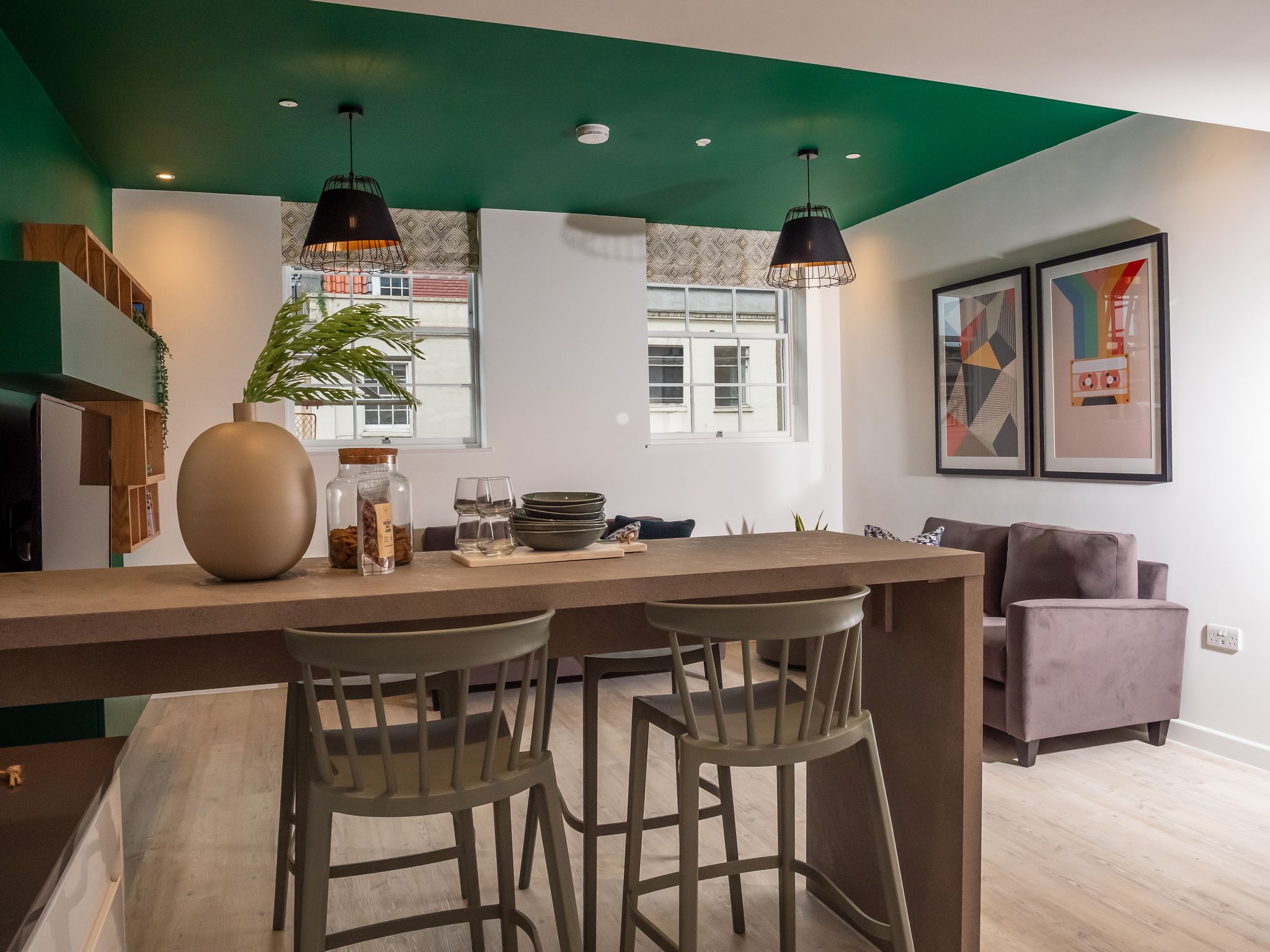 alt="student accommodation with bright green feature wall and flowing. ceiling, abstract prints and breakfast bar with plant"