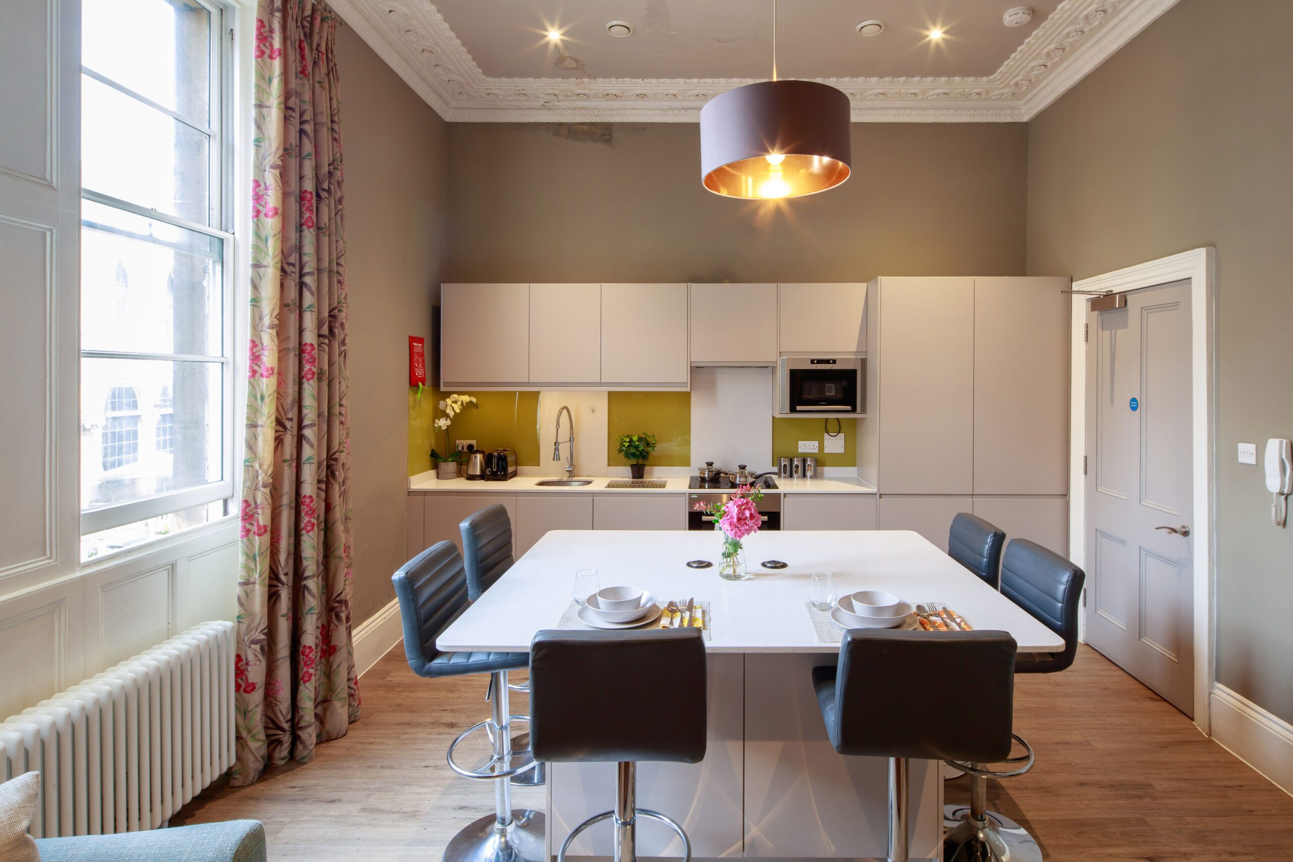 View of kitchen area with dining table, bar stools and white kitchenette.