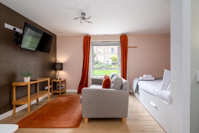 Living area in studio apartment at Alison Court. Red curtains with dark brown feature wall, sofa and tv.