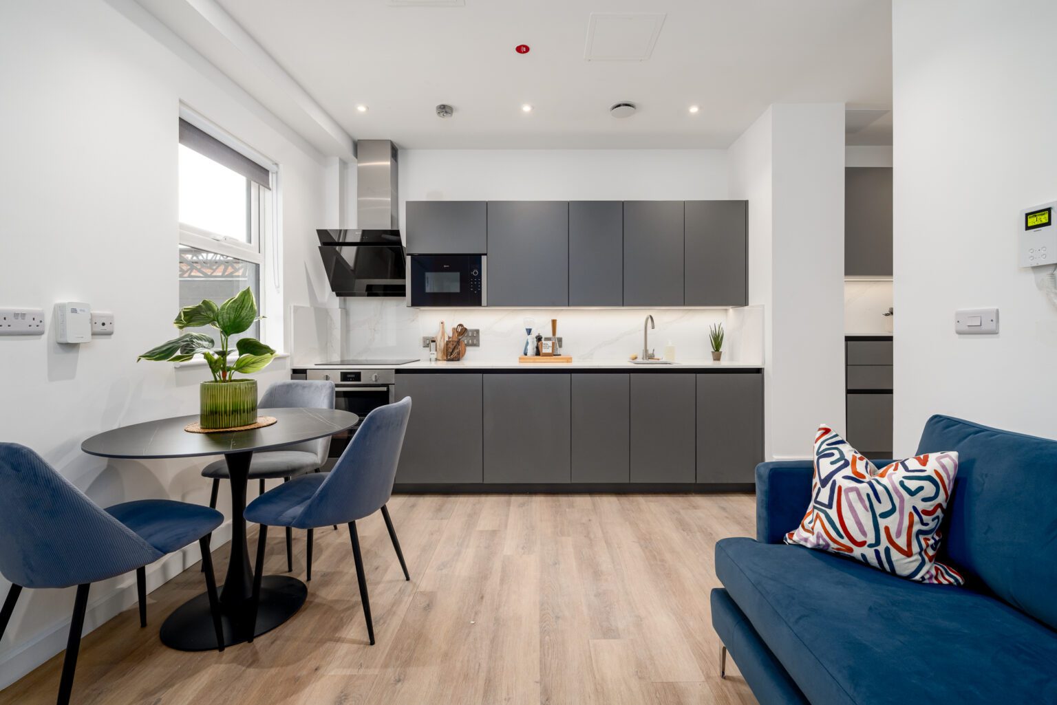 interior shot of living and kitchen area with grey kitchenette, glass dining table and blue sofa
