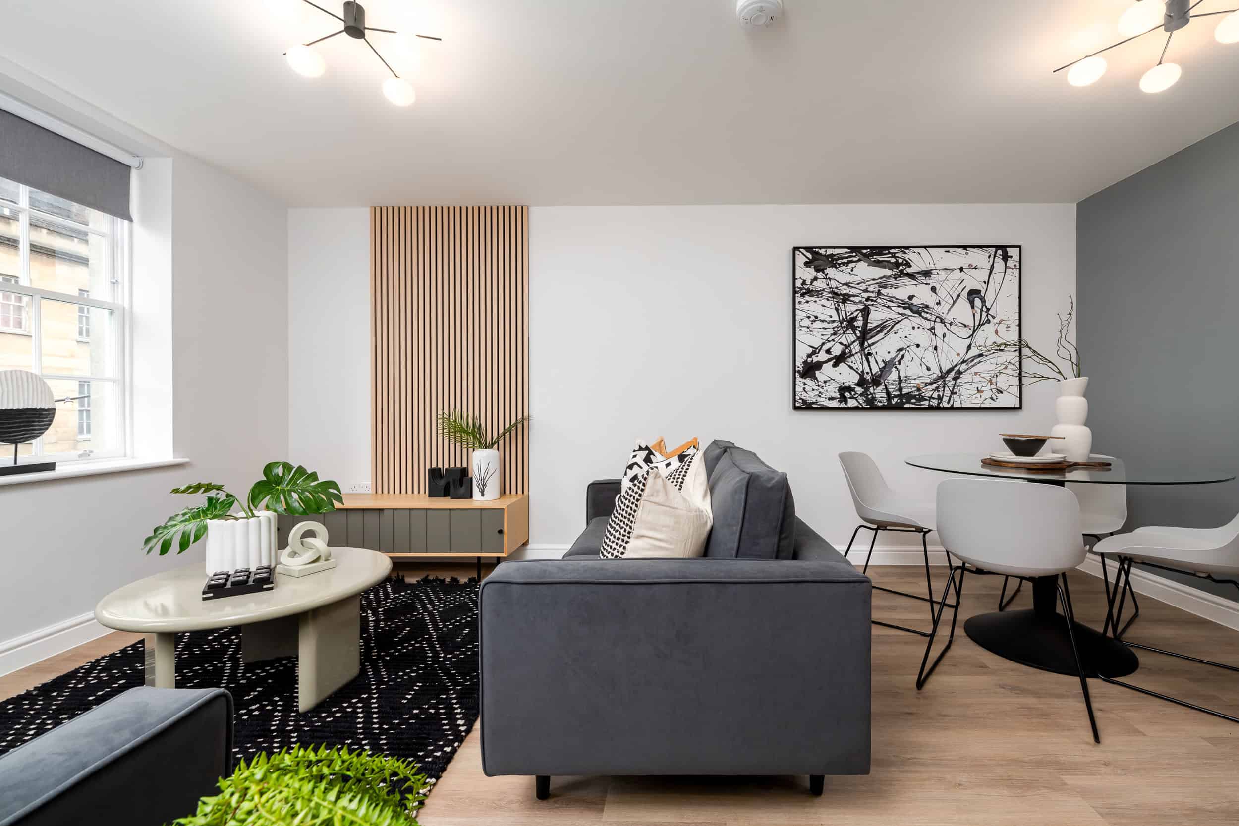 Side shot of living area with green sofa, grey artwork, feature wall and dining table.