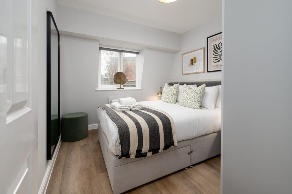 Bedroom with double bed with white linen, brown and cream throw and artwork above the bed.