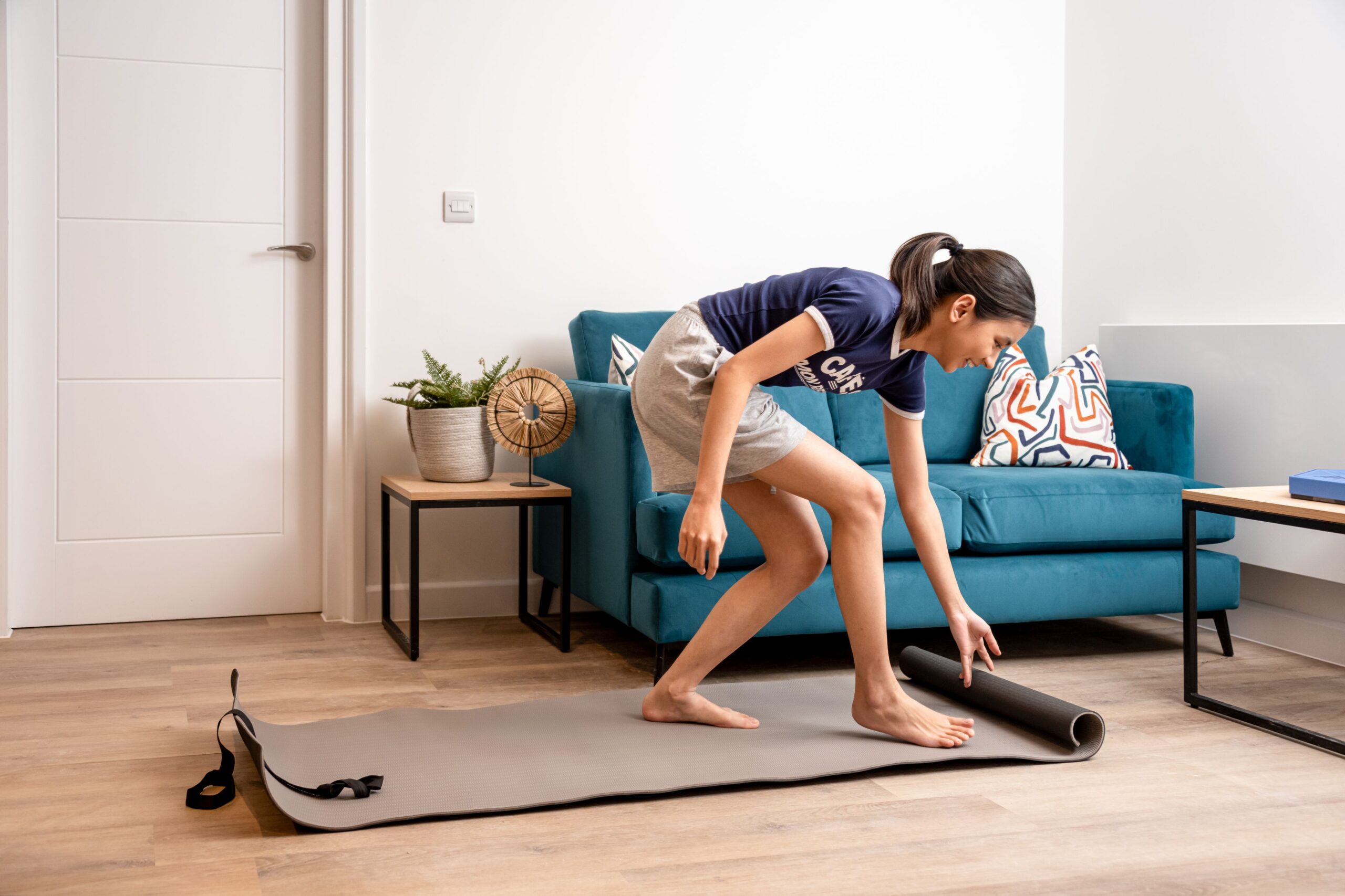 Girl placing yoga mat on floor with sofa and table in the background