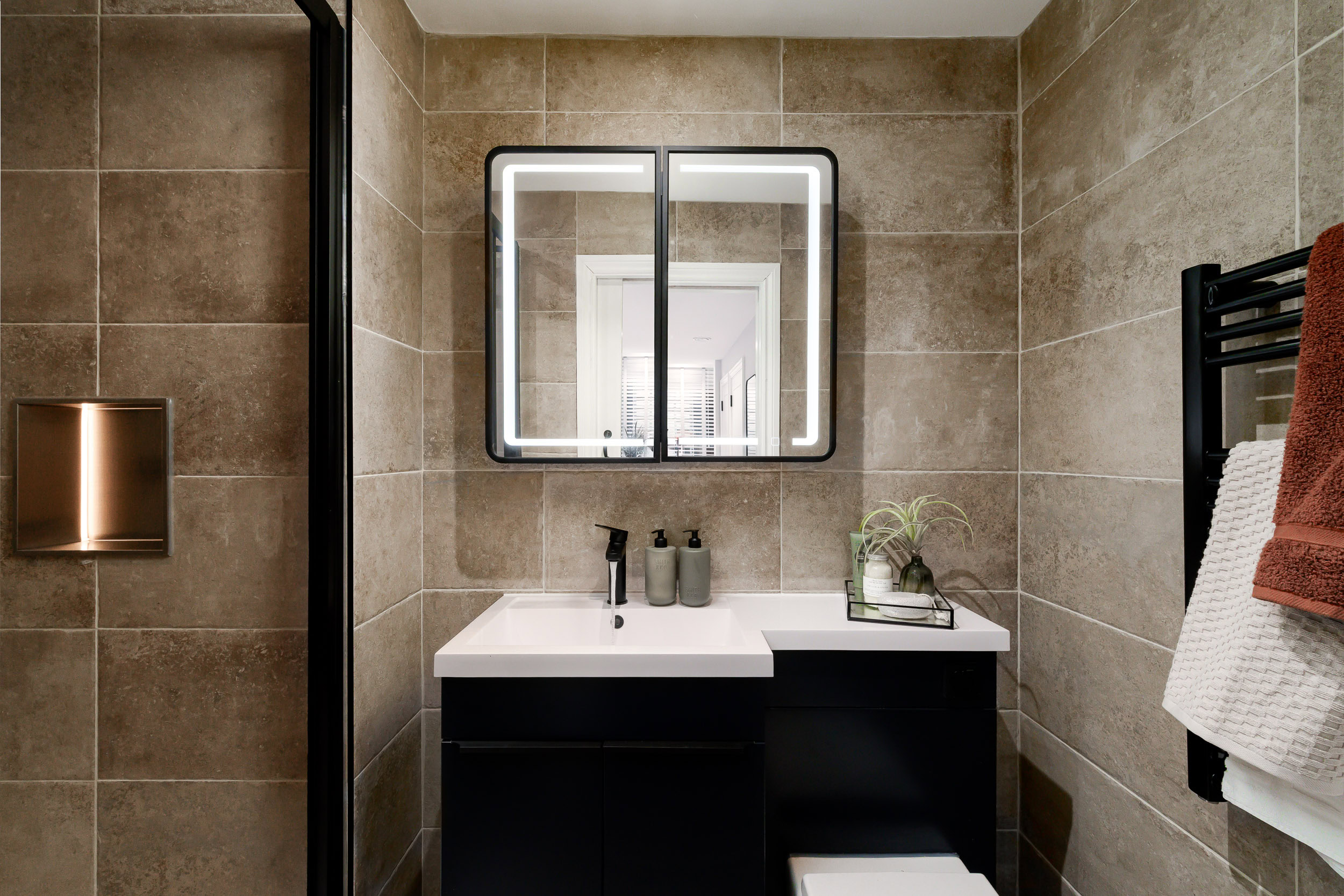 A bathroom featuring a sink, toilet, and a mirror above the sink, with neutral-colored walls and tiled flooring.
