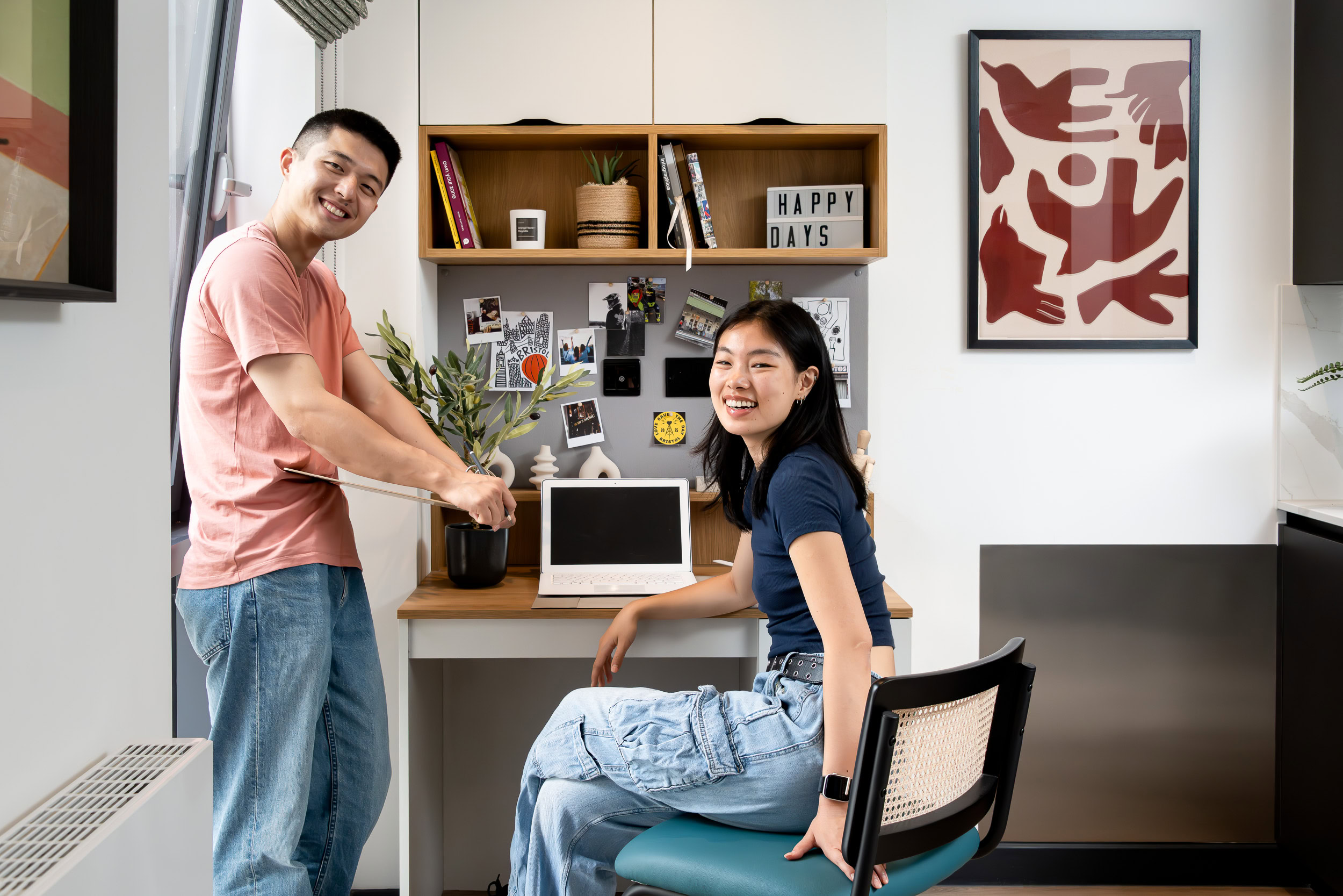 A man and woman sit at a desk in a small room, engaged in conversation or work.