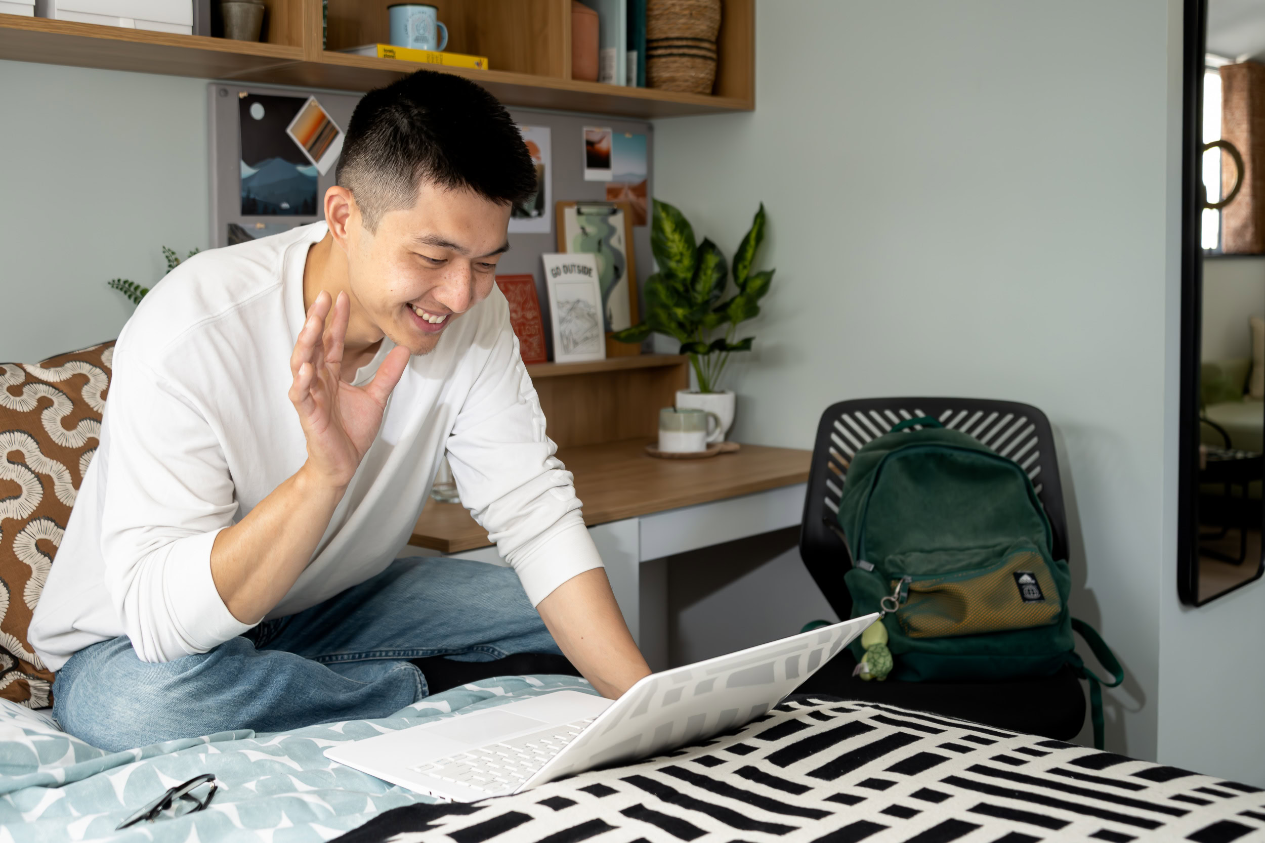 Man sitting on a bed, looking contemplative with a neutral expression in a softly lit bedroom.