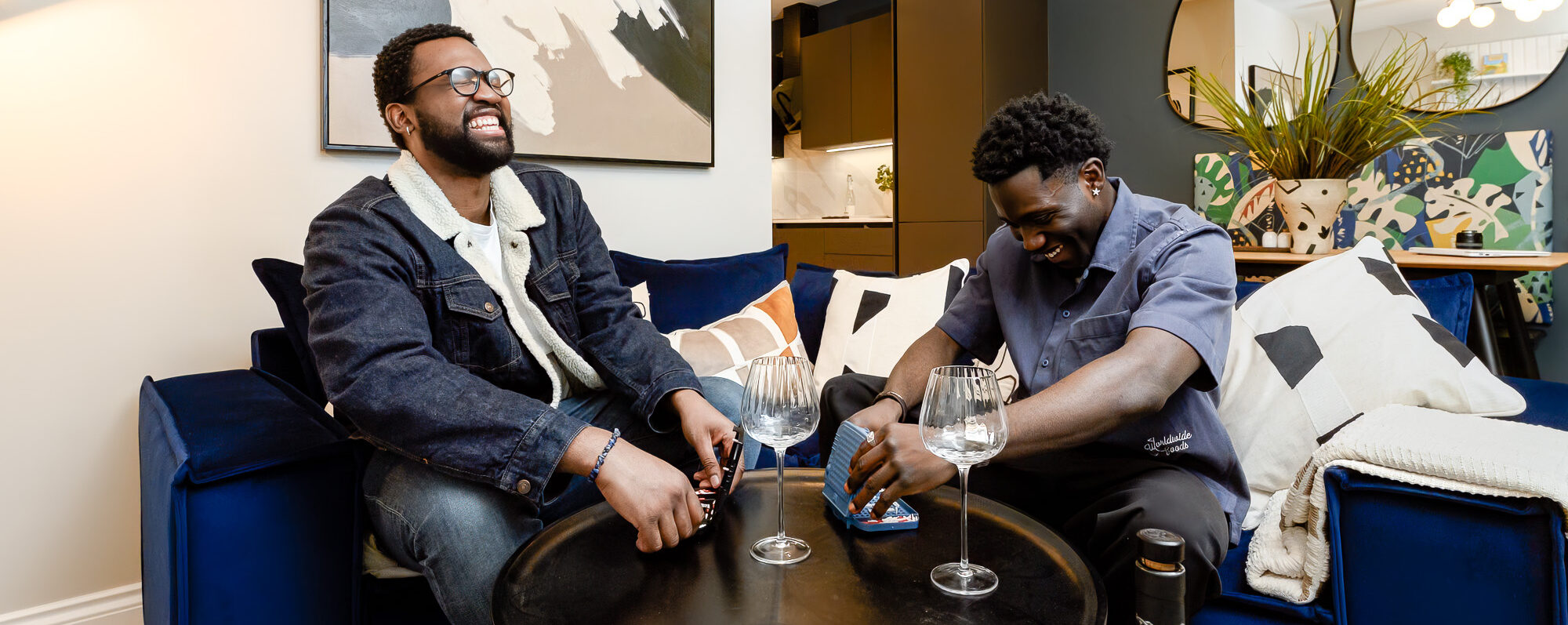 Side shot of living area with blue sofa, glass dining table and ornaments, feature wall and coffee table.
