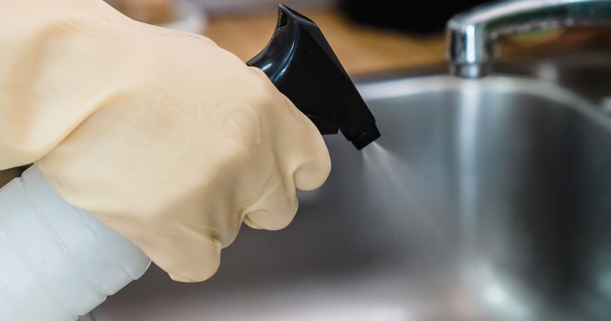A gloved hand cleans a kitchen sink with spray, showing the kind of housekeeping included in student accommodation.